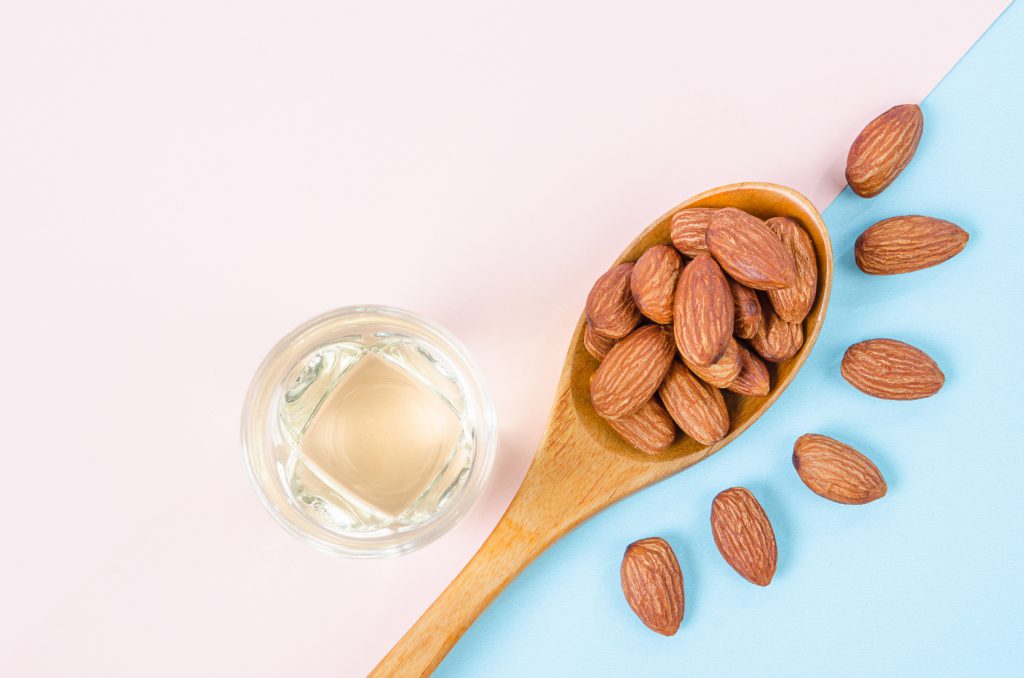 Peeled almonds seeds with almond oil on color paper background with empty space for your text or message.